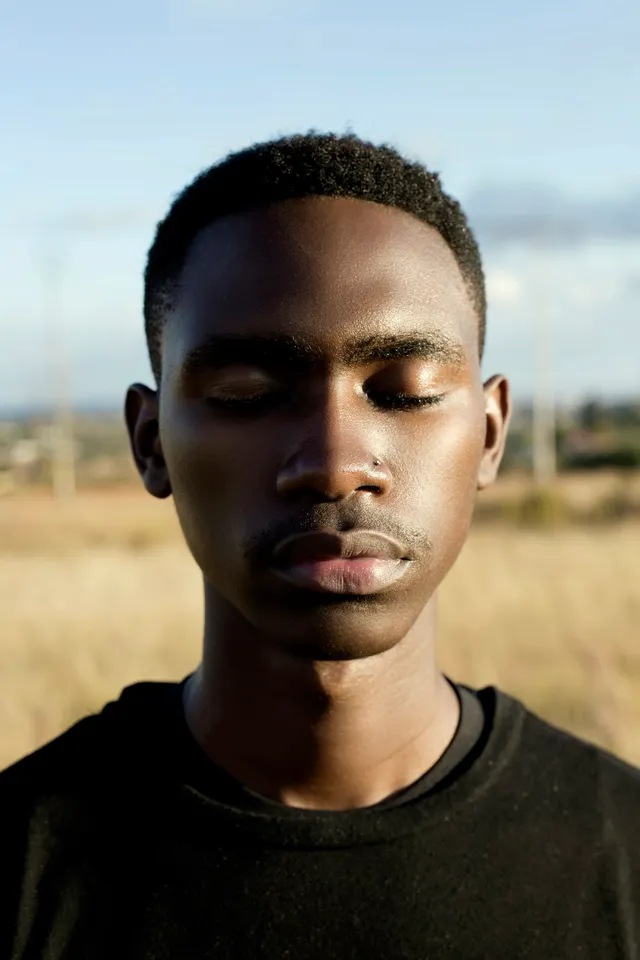 A young man sitting outdoors with his eyes closed, calm and centered